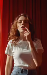 a beautiful woman wearing glasses, standing next to a red curtain