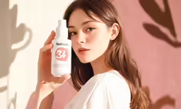 an asian woman is holding a jar of lotion and wearing a white shirt