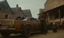 a man standing in front of a rusted car and singing into a microphone