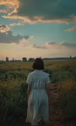 a girl walks down a dirt road toward a field of flowers