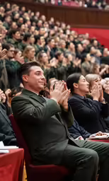 a man with a black suit sitting in front of some audience