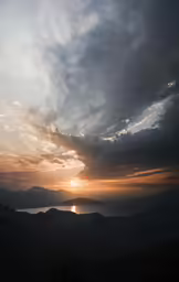 the sky is cloudy and the sun sets over some mountains