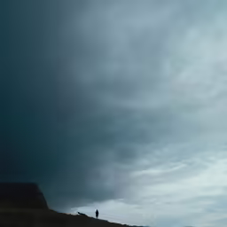 two people standing on a hill with dark clouds