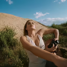 a woman standing with a camera next to a dune