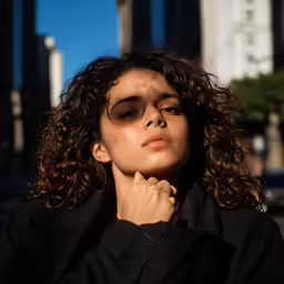 a woman with curly hair is looking down and has her hand on her chin