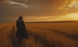 woman walking through a field during the sunset