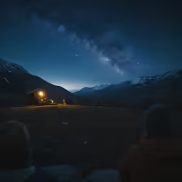 three people are watching a starlit night at the end of a mountain