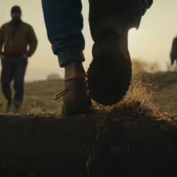 a person walking on some dirt in front of the sun