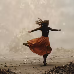 a young girl dances in an orange skirt on the beach