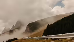 several empty road on the side of a hill with tall mountains in the background
