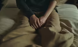 a woman sitting on top of a bed wearing brown pants