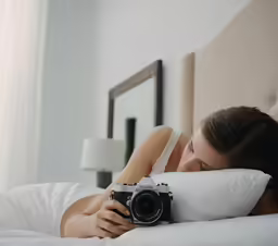 woman laying in bed with a camera and pillows