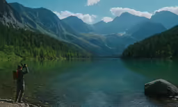 a person holding a camera up next to a lake