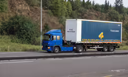 a semi truck with trailer driving on road next to forest,a semi truck is driving down the highway