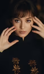 a woman with brown hair wearing black and gold sweater with her hands over her face