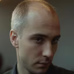 an adult man with bald head, staring at the camera