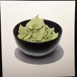 a black bowl filled with green leaves on top of a table