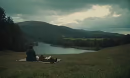 a woman and two dogs enjoying a picnic on a blanket overlooking a lake