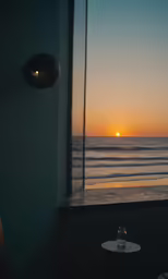 the sunset from a window overlooking the ocean and the beach