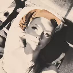 woman with white top on sitting on a bench and wearing tan towel