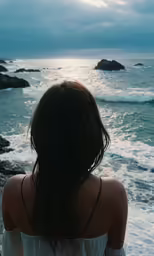 a woman wearing a white top looking out at the ocean
