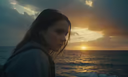 a woman is standing near the ocean at sunset
