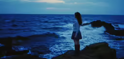 a girl stands on rocks near the ocean, and looks at something