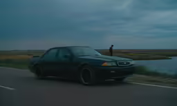 a man standing behind a black car while he drives