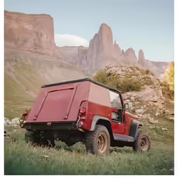 an old style red jeep is in the grass