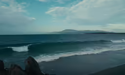 the blue sky shows dark clouds over some waves and a distant island