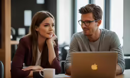 a man and woman looking at a laptop on the table