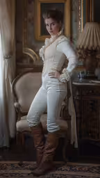 a woman standing next to a chair in a room,a woman wearing cowboy boots is posing for a photo