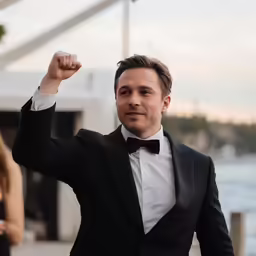 a man in a tuxedo waves to the crowd