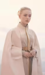 a young woman in an orange dress and long, cape stands near the ocean