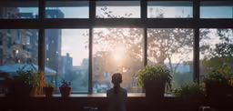 a woman sits in front of a large window and watches the sun go down
