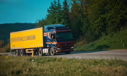 the bright yellow truck is driving along the road,a yellow and blue semi - truck driving on the road