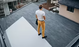 the man is looking at the building while standing on the roof