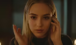 a blonde woman looking to her left while holding her hands near her face
