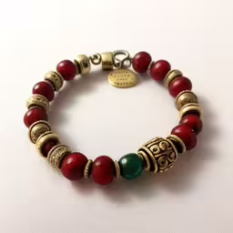 a red beaded bracelet with gold filigrees and a medallion,a bracelet with red and green beads is sitting on the table