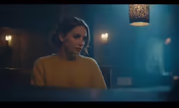 a girl in a yellow sweater looks serious in a darkened room