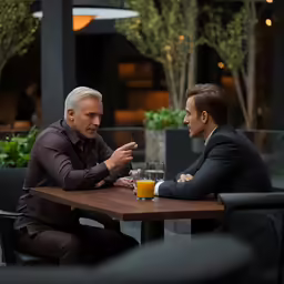 a man sitting at a table talking to another man