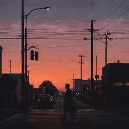 a person crossing a street at dusk with a car going by