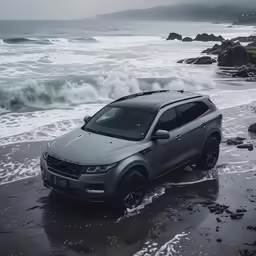 a silver suv is driving on the wet beach near waves