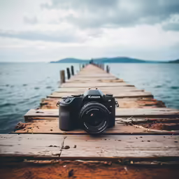camera on wooden pier with water and cloudy sky