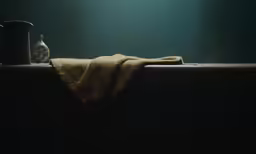 towels, an antique coffee pot and an old clock are lying on a table in the dark
