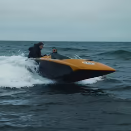 two men ride an orange and black boat on top of water