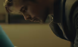 a man looking at his laptop screen while sitting on a bed