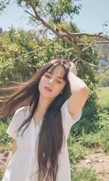 the young woman is posing near some trees