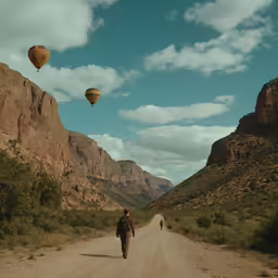two people walking down a dirt road in the mountains
