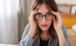 a woman wearing a blue shirt and glasses holding her hand on her face